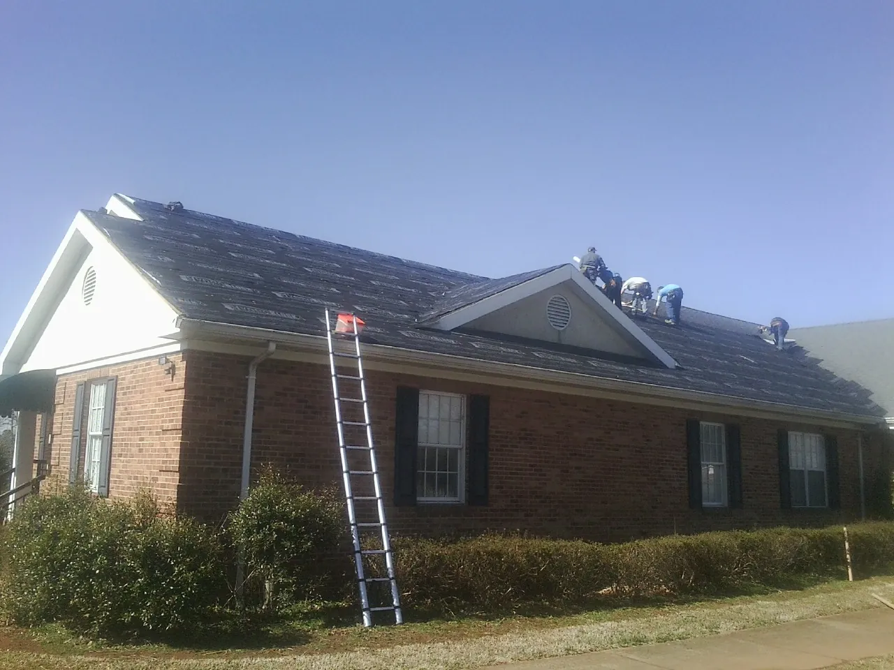 Crew tearing shingles off a brick ranch roof with a ladder set — Metal Roof Repair work by our crew in Blacksburg
