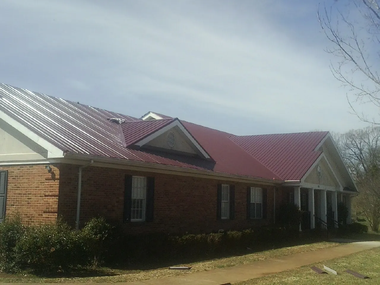 Red metal roof with gabled entries on a long brick building, from a Hail Damage Roof Repair job in Blacksburg