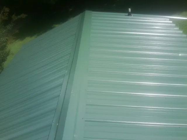 New green metal panels meeting at the ridge of a roof — Flat Roof Repair work by our crew in Blacksburg